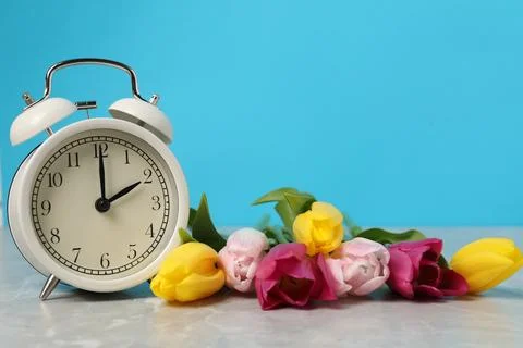 Spring time. Alarm clock and beautiful tulips on grey marble table against .. Foto stock