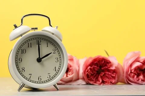 Spring time. Alarm clock and beautiful flowers on grey marble table against.. Stock Photos