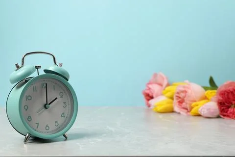 Spring time. Alarm clock and beautiful flowers on grey marble table against.. Stock Photos