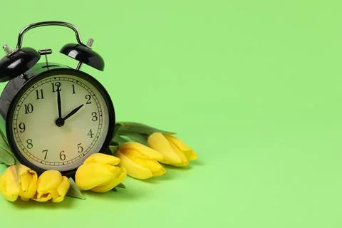 Spring time. Alarm clock and beautiful tulips on green background, space fo.. Stock Photos