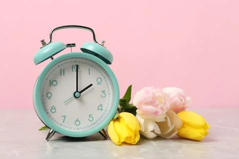 Spring time. Alarm clock and beautiful tulips on grey marble table against .. 스톡 사진