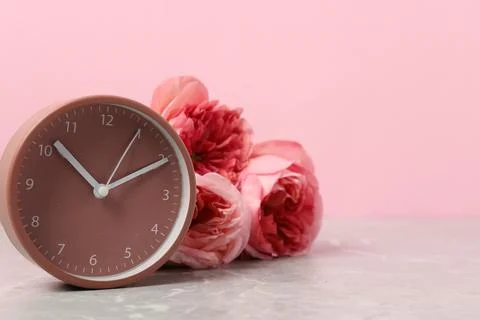 Spring time. Alarm clock and beautiful roses on grey marble table against p.. Foto stock