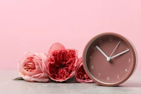 Spring time. Alarm clock and beautiful roses on grey marble table against p.. Stock Photos