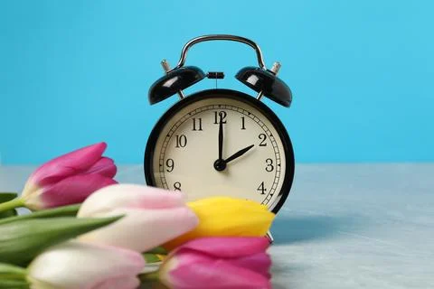 Spring time. Alarm clock and beautiful tulips on grey marble table against .. 스톡 사진