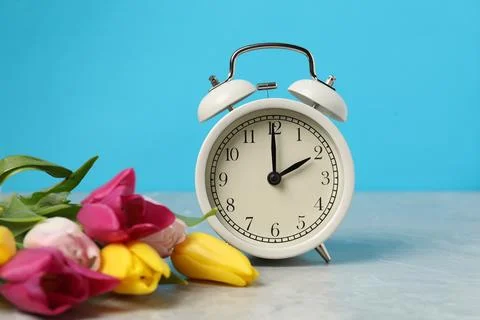 Spring time. Alarm clock and beautiful tulips on grey marble table against .. Foto stock