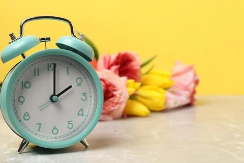 Spring time. Alarm clock and beautiful flowers on grey marble table against.. 写真素材