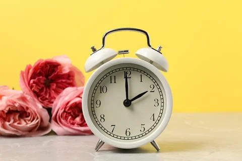 Spring time. Alarm clock and beautiful roses on grey marble table against y.. Foto stock