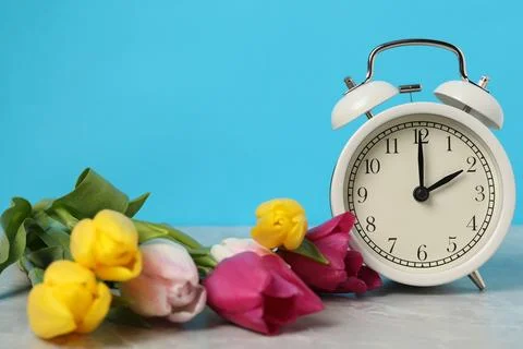 Spring time. Alarm clock and beautiful tulips on grey marble table against .. 写真素材
