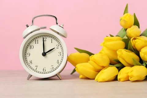 Spring time. Alarm clock and beautiful tulips on wooden table against pink .. Stock Photos