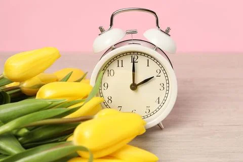 Spring time. Alarm clock and beautiful tulips on wooden table against pink .. Stock Photos