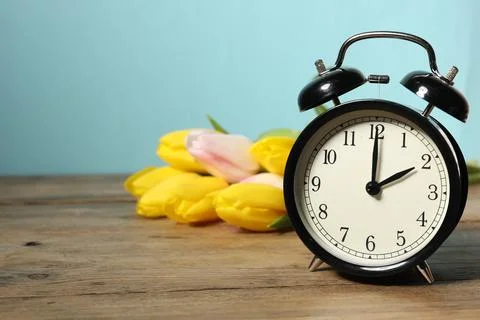 Spring time. Alarm clock and beautiful tulips on wooden table against light.. Foto stock