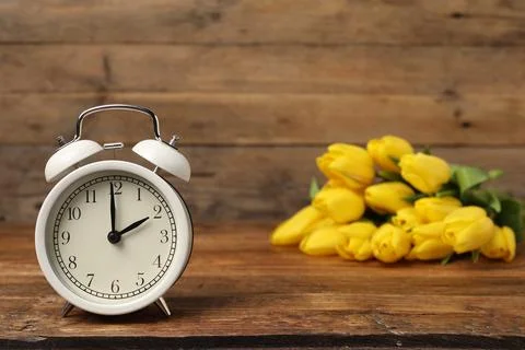 Spring time. Alarm clock and beautiful tulips on wooden table Foto stock