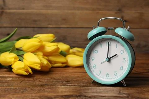 Spring time. Alarm clock and beautiful tulips on wooden table Stock Photos