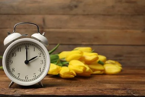 Spring time. Alarm clock and beautiful tulips on wooden table Stock Photos