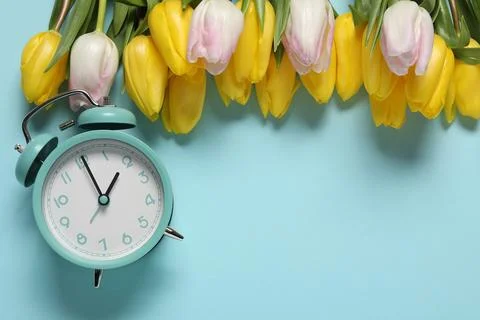 Spring time. Alarm clock and beautiful tulips on light blue background, fla.. Foto stock