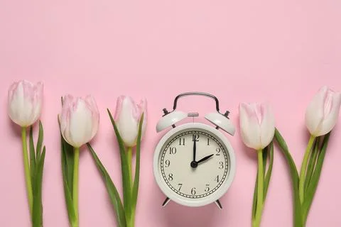 Spring time. Alarm clock and beautiful tulips on pink background, flat lay... Stock Photos