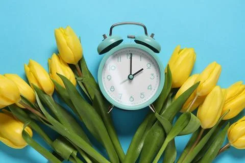 Spring time. Alarm clock and beautiful tulips on light blue background, fla.. Stock Photos