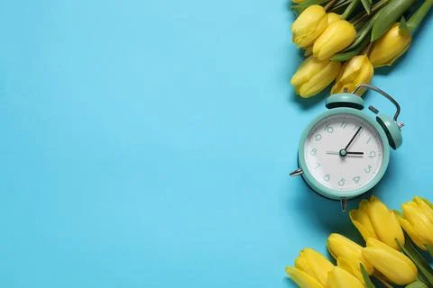 Spring time. Alarm clock and beautiful tulips on light blue background, fla.. 写真素材
