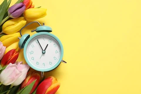 Spring time. Alarm clock and beautiful tulips on yellow background, flat la.. 写真素材