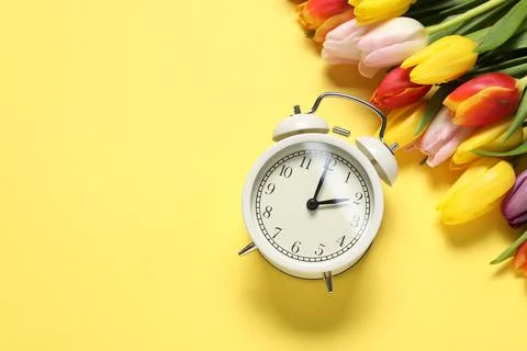 Spring time. Alarm clock and beautiful tulips on yellow background, flat la.. Foto stock