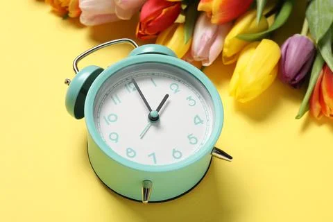 Spring time. Alarm clock and beautiful tulips on yellow background, closeup Stock Photos