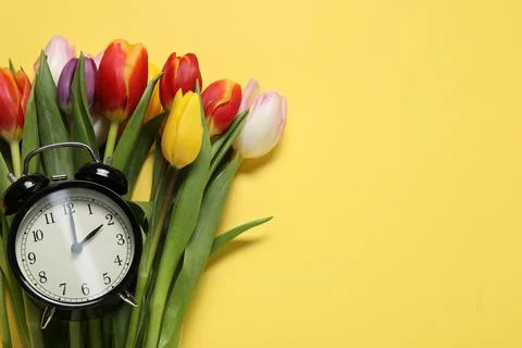 Spring time. Alarm clock and beautiful tulips on yellow background, flat la.. 写真素材
