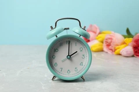 Spring time. Alarm clock and beautiful flowers on grey marble table against.. 写真素材