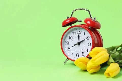 Spring time. Alarm clock and beautiful tulips on green background, space fo.. Stock Photos