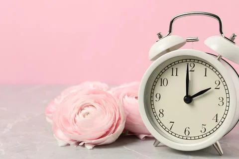 Spring time. Alarm clock and beautiful ranunculus flowers on grey marble ta.. Stock Photos