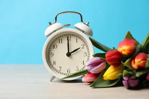 Spring time. Alarm clock and beautiful tulips on wooden table against light.. 스톡 사진