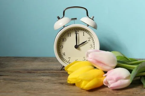 Spring time. Alarm clock and beautiful tulips on wooden table against light.. 스톡 사진