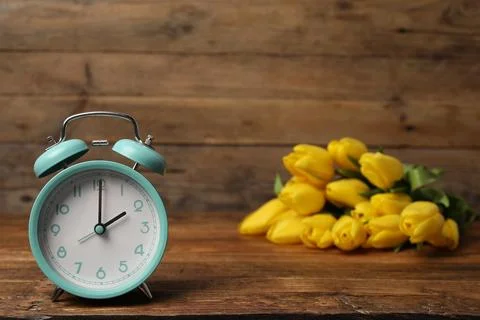 Spring time. Alarm clock and beautiful tulips on wooden table Stock Photos