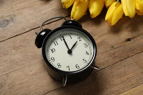 Spring time. Alarm clock and beautiful tulips on wooden table, above view Foto stock