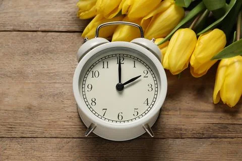 Spring time. Alarm clock and beautiful tulips on wooden table, above view Foto stock