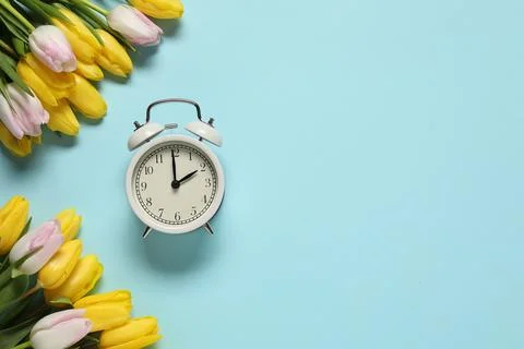 Spring time. Alarm clock and beautiful tulips on light blue background, fla.. Stock Photos