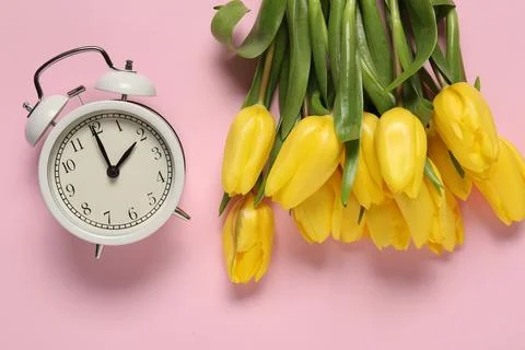 Spring time. Alarm clock and beautiful tulips on pink background, flat lay 스톡 사진
