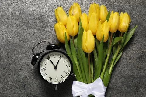 Spring time. Alarm clock and beautiful tulips on grey table, flat lay Stock Photos