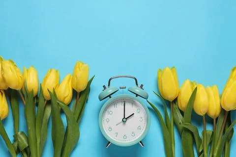 Spring time. Alarm clock and beautiful tulips on light blue background, fla.. 写真素材