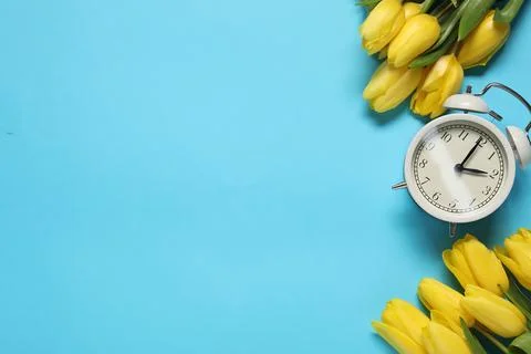 Spring time. Alarm clock and beautiful tulips on light blue background, fla.. 스톡 사진