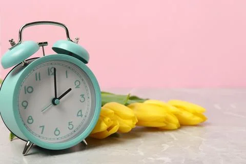 Spring time. Alarm clock and beautiful tulips on grey marble table against .. Foto stock