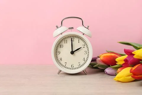 Spring time. Alarm clock and beautiful tulips on wooden table against pink .. 스톡 사진