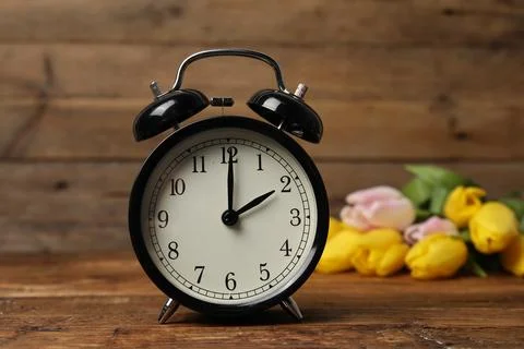 Spring time. Alarm clock and beautiful tulips on wooden table Foto stock
