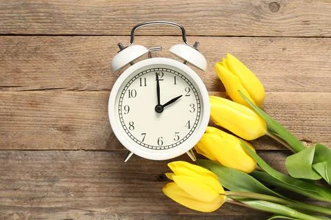 Spring time. Alarm clock and beautiful tulips on wooden table, flat lay Stock Photos