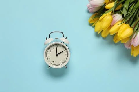 Spring time. Alarm clock and beautiful tulips on light blue background, fla.. 스톡 사진