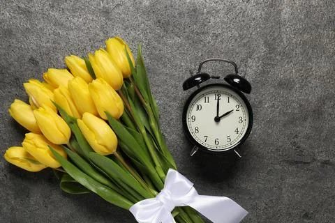 Spring time. Alarm clock and beautiful tulips on grey table, flat lay Stock Photos