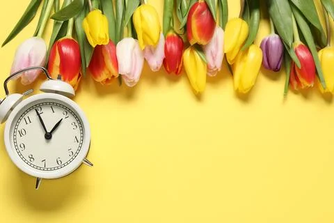 Spring time. Alarm clock and beautiful tulips on yellow background, flat la.. Foto stock