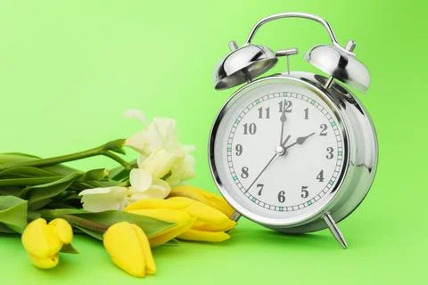 Spring time. Alarm clock and beautiful flowers on green background 스톡 사진