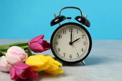 Spring time. Alarm clock and beautiful tulips on grey marble table against .. 스톡 사진
