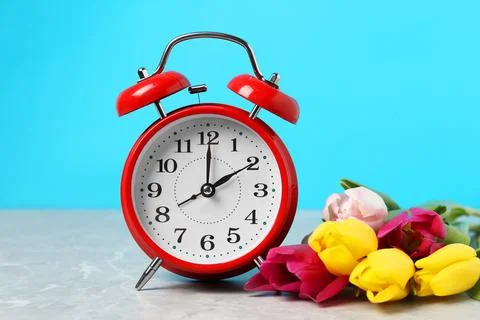 Spring time. Alarm clock and beautiful tulips on grey marble table against .. Stock Photos