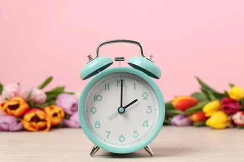 Spring time. Alarm clock and beautiful tulips on wooden table against pink .. Foto stock